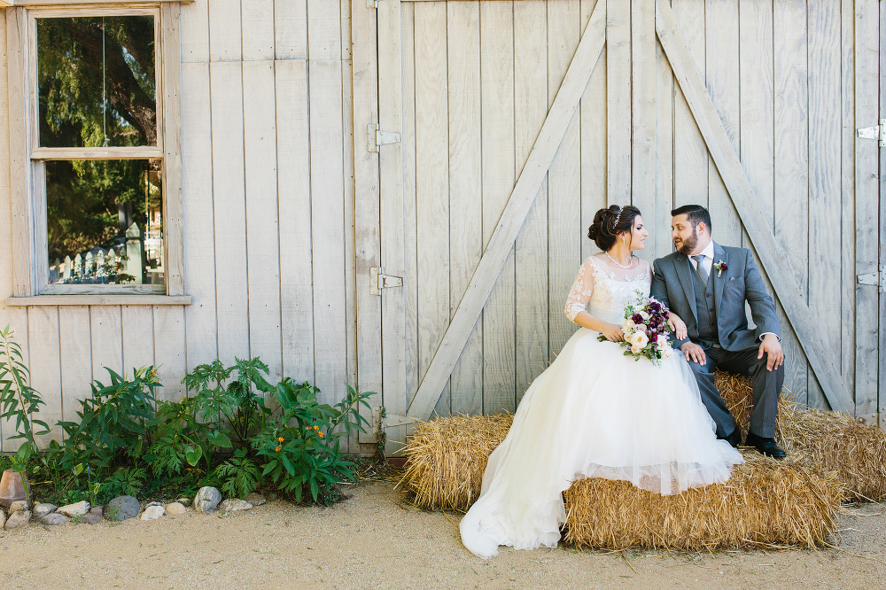 The bride and groom sitting on haybails. 